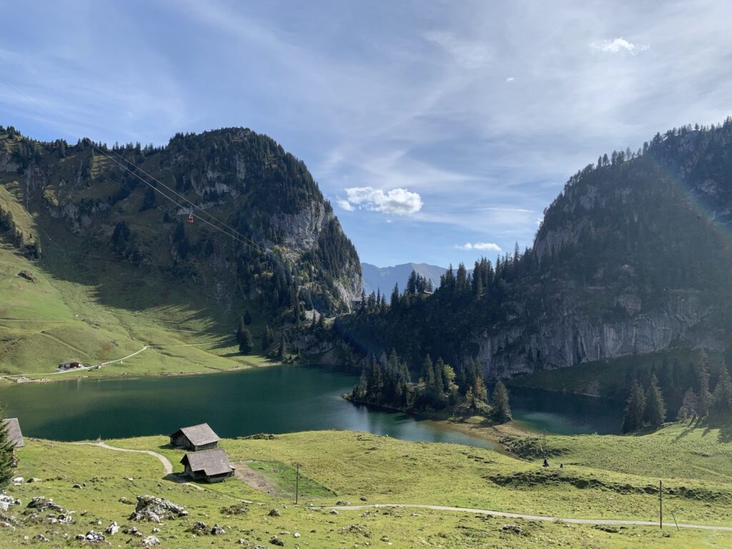 Panorama auf den Hinterstockensee mit Alphütten im Vordergrund und Seilbahn im Hintergrund.