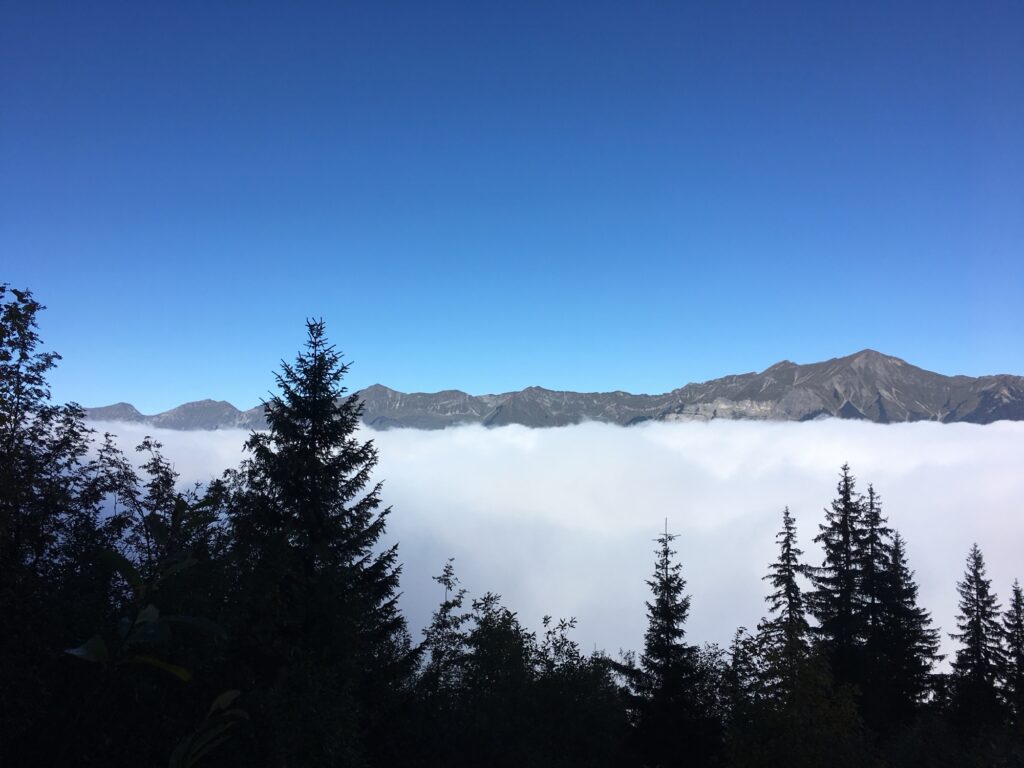Weite Aussicht auf Bergkette über Nebelmeer, blauer Himmel ohne Wolken.