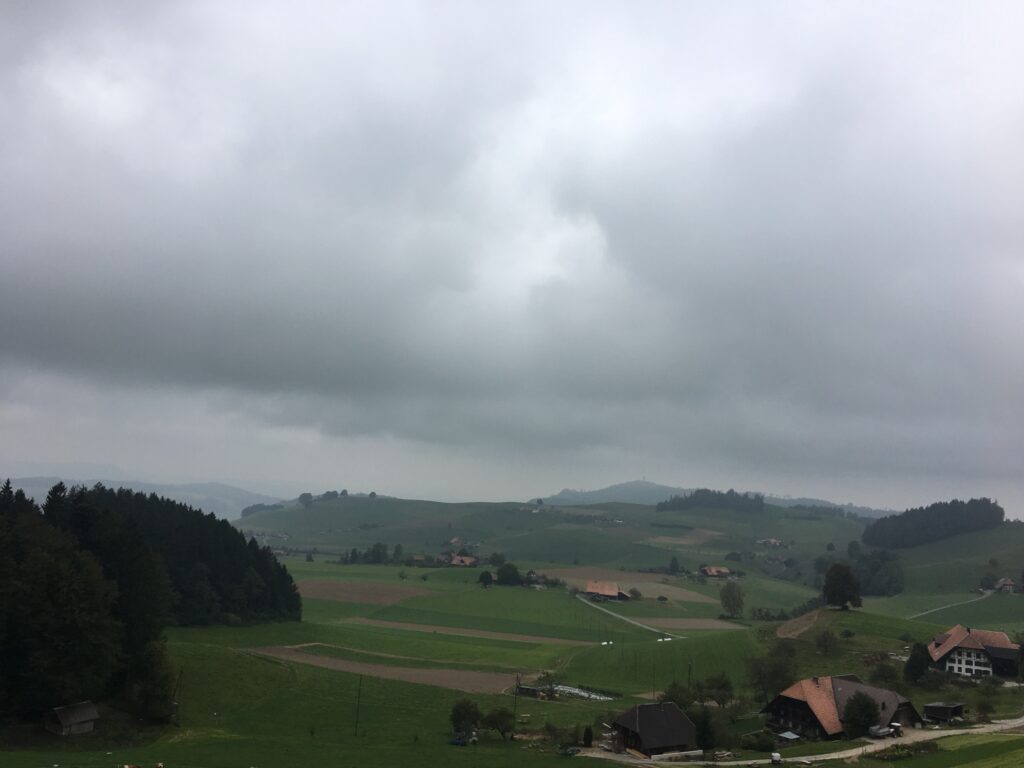 Blick über die sanften Hügel des Emmentals, dunkle Wälder im Vordergrund und tiefe Wolkendecke.