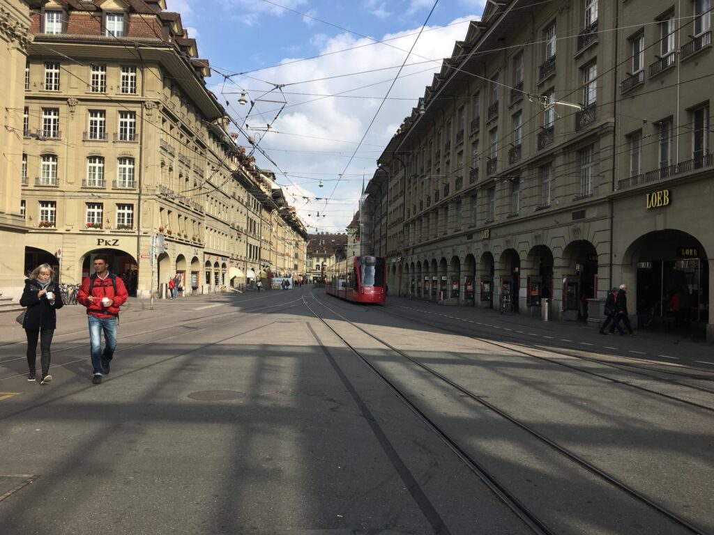 Belebte Berner Altstadt mit Tram, Passanten und historischen Gebäuden entlang der Einkaufsstrasse.