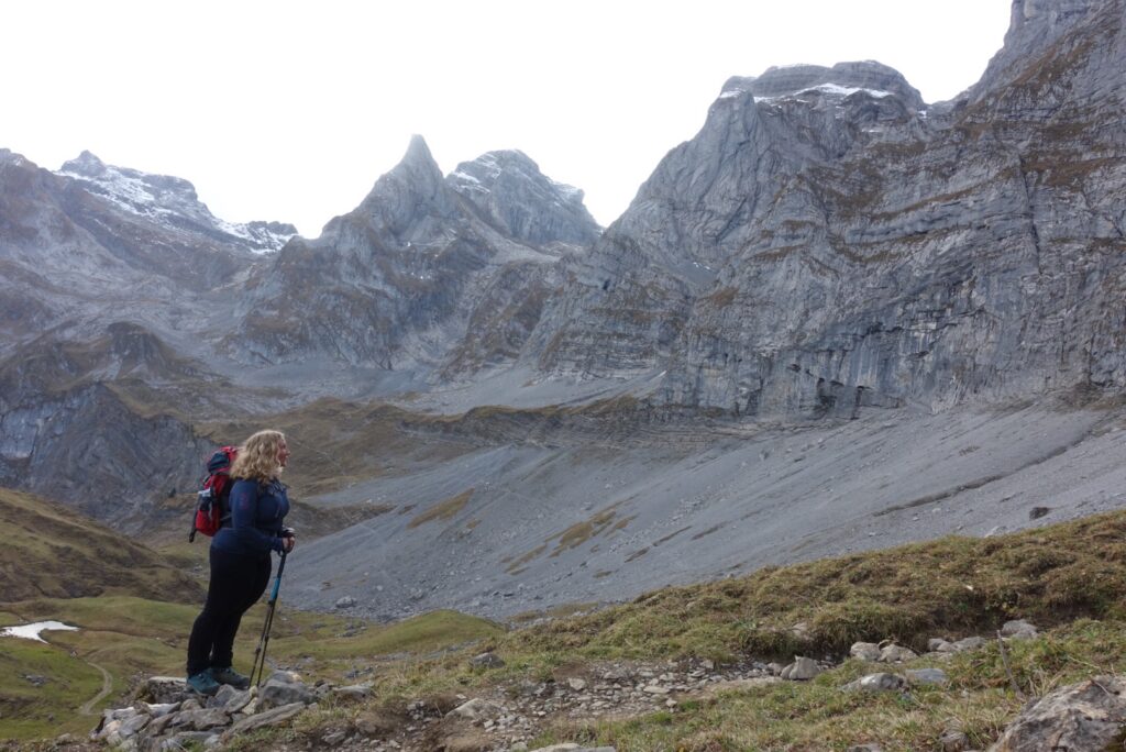 Wanderin blickt auf karge graue Felswände und schroffe Bergspitzen in hochalpiner Landschaft.