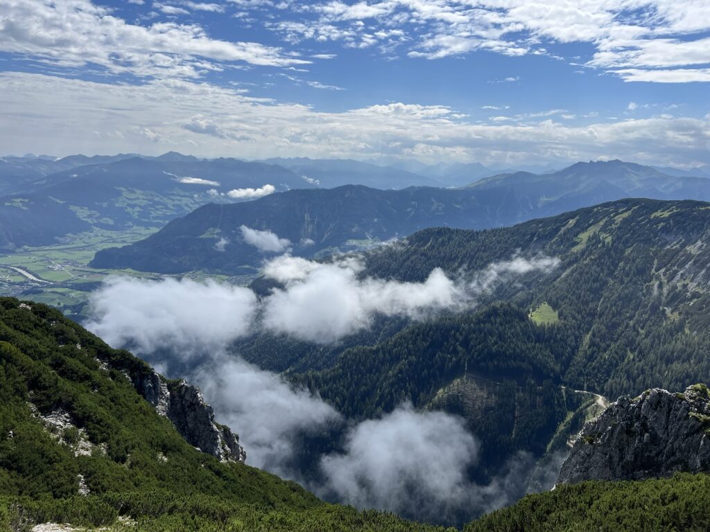 Tiefblick ins Inntal: Wolkenfetzen ziehen über die bewaldeten Hänge, weite grüne Landschaft bis zum Horizont sichtbar.