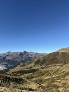 Weite Berglandschaft mit Blick Richtung Simmental – sanfte Hänge, klare Herbstfarben und wolkenloser Himmel über den Berner Alpen.