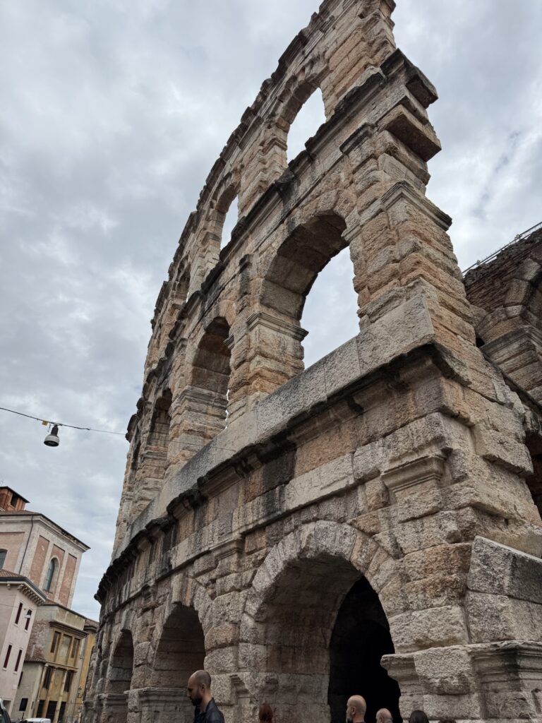 Detailaufnahme der Arena di Verona mit ihren markanten römischen Bögen unter einem wolkigen Himmel.