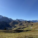 Panoramablick über das grüne Tal Richtung Adelboden – sanfte Hügel und erste Schneereste auf den Gipfeln.