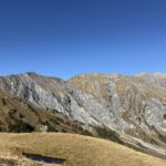 Kleine Wasserfläche inmitten goldener Wiesen – Spiegelung der Felsen und blauer Himmel, ruhige Bergstimmung.