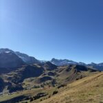 Aussicht auf das sonnige Alptal unterhalb des Silerbühls – goldene Wiesen und schneebedeckte Gipfel in der Ferne.