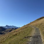 Wanderweg am steilen Grashang mit Blick auf die schneebedeckten Alpen – sanfter Aufstieg Richtung Silerbühl unter klarem Herbsthimmel.