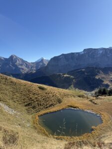 Kleiner Bergsee unterhalb der Felsen am Hahnenmoospass – ruhige Spiegelung und herbstliche Farben mit Blick auf die Berner Alpen.