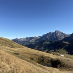 Aussicht über die Hänge des Hahnenmoospasses – goldene Gräser, kleiner Weiher und majestätische Bergkulisse im Hintergrund.