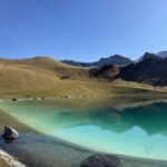 Kristallklarer Bergsee mit türkisfarbenem Wasser – Spiegelung der Hügel und Gipfel bei Sonnenschein, oberhalb des Hahnenmoospasses.