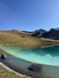 Kristallklarer Bergsee mit türkisfarbenem Wasser – Spiegelung der Hügel und Gipfel bei Sonnenschein, oberhalb des Hahnenmoospasses.