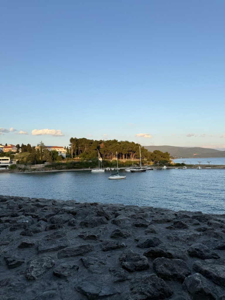 Yachthafen mit Segelbooten und kleiner bewaldeter Halbinsel im goldenen Abendlicht auf Krk.