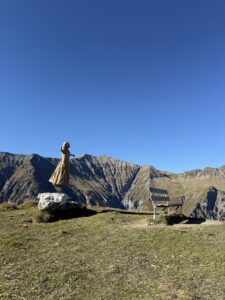 Vogel-Lisi-Statue auf Felsblock neben Bank – beliebter Aussichtspunkt oberhalb Adelboden mit Panoramablick auf die Berglandschaft.