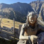 Sitzende Holzfigur der Vogel-Lisi auf Bank – kunstvolle Schnitzerei vor der Kulisse der steilen Felsen des Engstligentals.