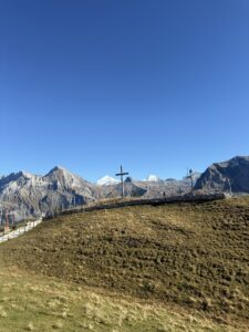 Kreuz und Wanderweg mit Alpenpanorama – herbstliche Berglandschaft am Hahnenmoospass bei klarer Fernsicht.