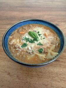 Herzhafte Lasagnesuppe mit Farfalle, Gemüse und Parmesan in einer blauen Keramikschale – cremig, würzig und ideal fürs Vanlife oder Mealprep