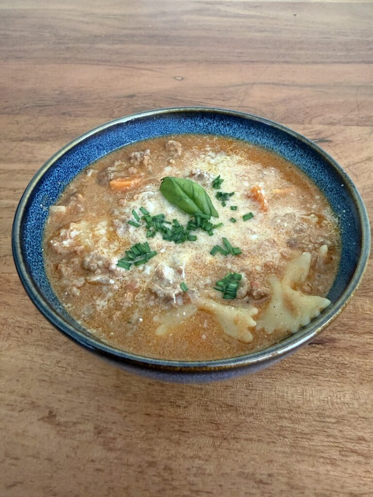 Herzhafte Lasagnesuppe mit Farfalle, Gemüse und Parmesan in einer blauen Keramikschale – cremig, würzig und ideal fürs Vanlife oder Mealprep