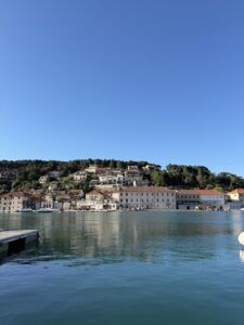 Blick auf den Hafen von Jelsa mit hellen Häusern und roten Dächern, die sich im ruhigen Wasser spiegeln.