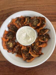 Ofengebackene Smashed-Parmesan-Kürbisstücke, goldbraun überbacken und mit Gewürzen bestreut, serviert mit Kräuterdip auf einem weissen Teller – herbstlich, würzig und einfach gemacht.