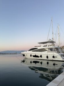 Weisse Yacht im Abendlicht, vertäut im Hafen von Jelsa mit sanftem Himmel im Hintergrund.