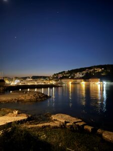 Nachtaufnahme von Jelsa – beleuchtete Uferpromenade und spiegelnde Lichter im Wasser unter klarem Sternenhimmel.