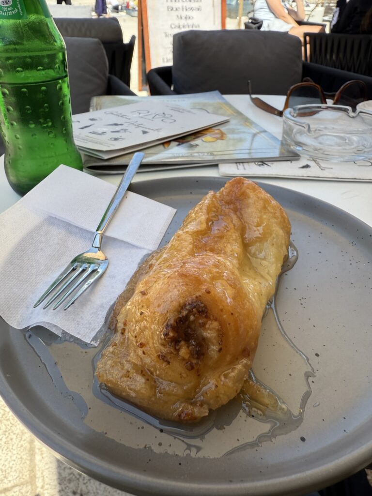 Dessert mit Honigglasur auf einem Teller im Café, daneben eine grüne Glasflasche und eine Karte.