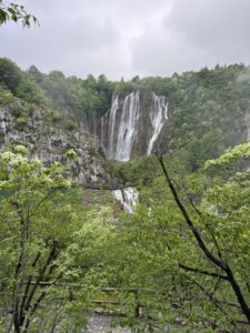 Majestätischer Wasserfall im Nationalpark Plitvicer Seen in Kroatien, umgeben von dichtem Grün und Felsen – ein beeindruckendes Naturhighlight bei leicht bewölktem Wetter.