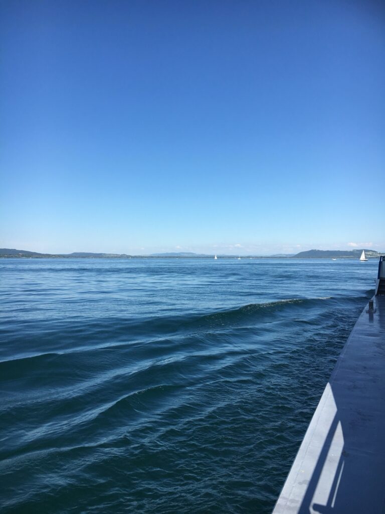 Bootsfahrt Neuenburgersee: Blauer Himmel und sanfte Wellen, aufgenommen vom Bootsrumpf mit Blick über den Neuenburgersee.