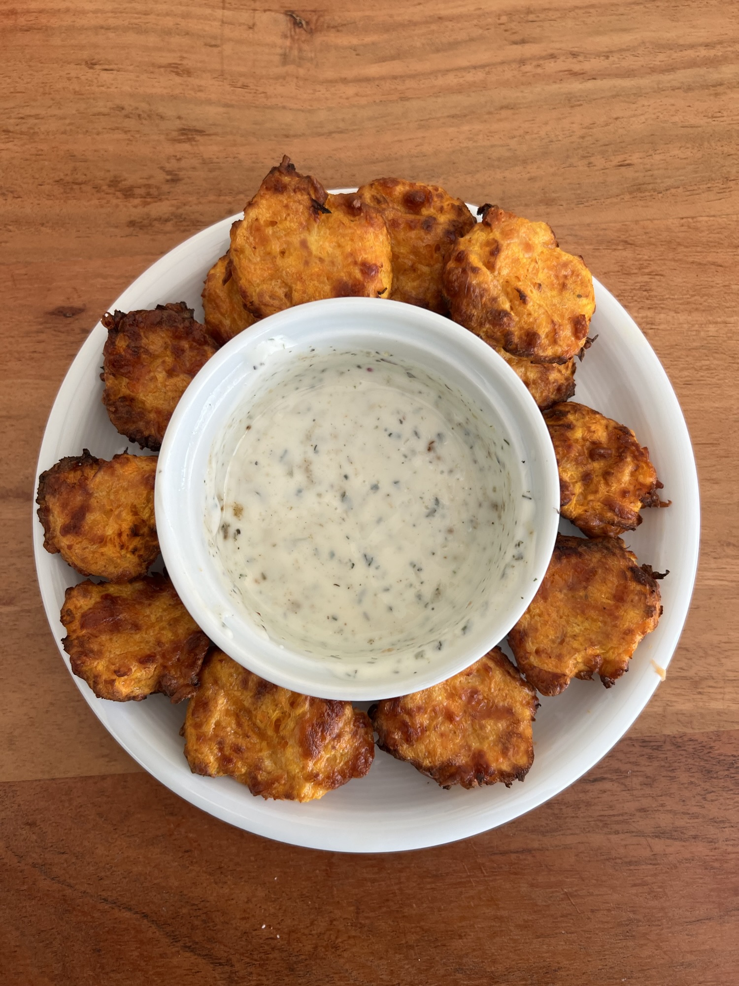 Hausgemachte Kürbis-Parmesan-Taler auf einem weissen Teller, angerichtet mit einem cremigen Kräuterdip in der Mitte – ein herbstlicher Snack mit knuspriger Kruste.