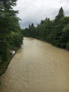 Blick über die Emme nach einem Regentag – braunes, fliessendes Wasser umgeben von sattem Grün.