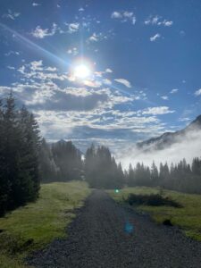 Schotterweg Richtung Weißbachsattel: Morgensonne bricht durch Wolken und Nebelschwaden, mystische Lichtstimmung in den Bergen.