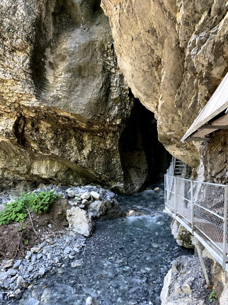 Eingang zur Cholerenschlucht Adelboden mit Steg und Felsüberhang über klarem Wasser.