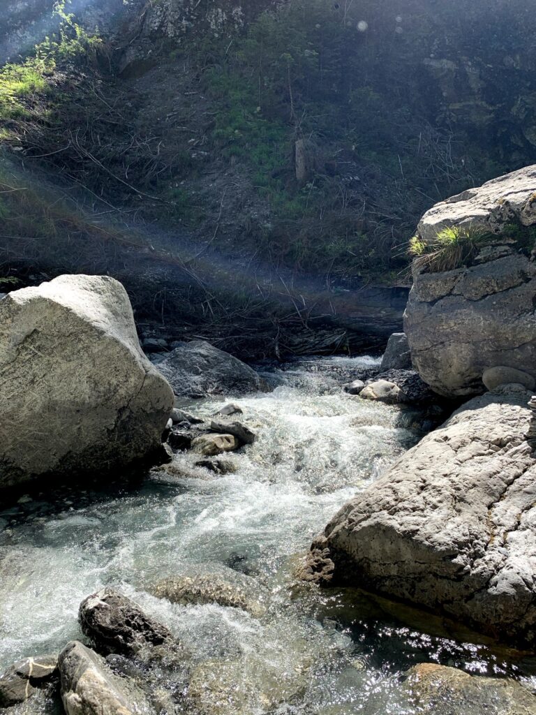 Gebirgsbach im Sonnenschein – Sprudelndes, türkisfarbenes Wasser fliesst zwischen grossen Felsblöcken durch die Schlucht.