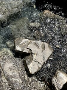 Herzförmiger Stein im klaren Wasser – Sonnenstrahlen glitzern auf der Wasseroberfläche rund um einen herzförmigen Stein.