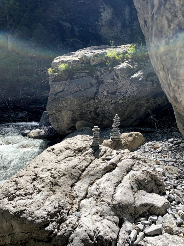 Steinmännchen am Flussufer – Zwei kleine Steintürme stehen auf einem grossen, hellen Felsen am Wasserlauf.