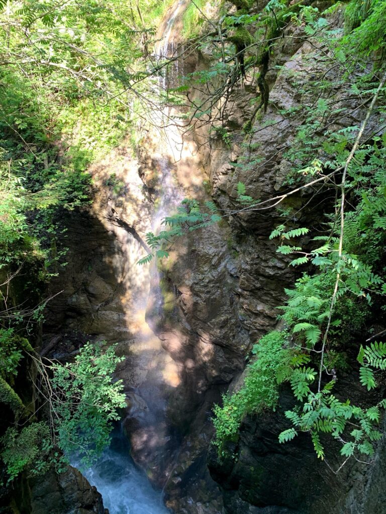 Wasserfall in einer Felsenschlucht – Sonnenlicht fällt auf das herabstürzende Wasser zwischen hohen, moosbewachsenen Felsen.