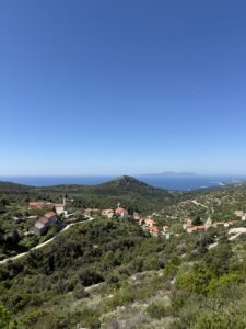 Panoramablick auf die Hügellandschaft bei Stari Grad auf der Insel Hvar in Kroatien mit traditionellen Steinhäusern und roten Ziegeldächern, umgeben von mediterraner Vegetation und Blick aufs tiefblaue Meer unter klarem Himmel.