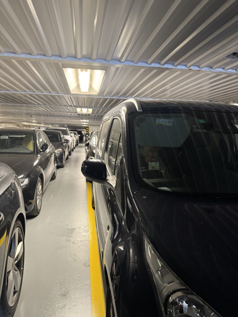 Autos stehen eng parkiert im unteren Fahrzeugdeck einer Fähre auf der Route in Kroatien, mit künstlicher Beleuchtung und wenig Platz zwischen den Reihen