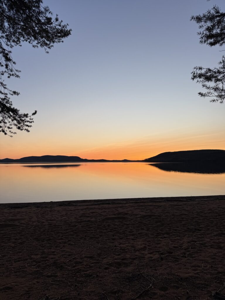 Sonnenuntergang am See in Lappland – Der Himmel leuchtet in Orange und Rosa, das Wasser liegt spiegelglatt – ein stiller Abend in der Natur.
