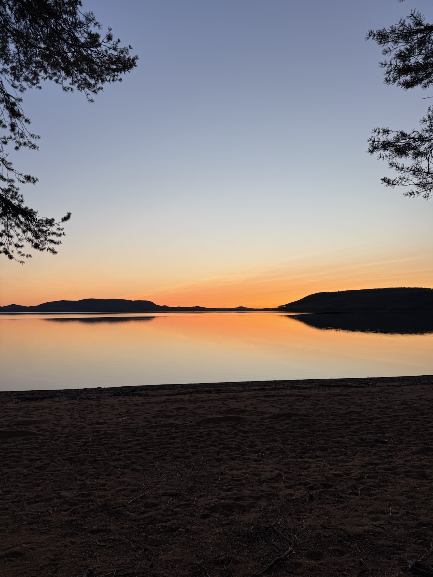 Sonnenuntergang am See in Lappland – Der Himmel leuchtet in Orange und Rosa, das Wasser liegt spiegelglatt – ein stiller Abend in der Natur.