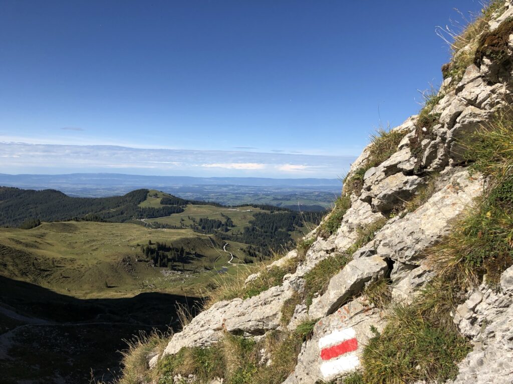 Aussicht vom Morgetepass über die Voralpen bis zum Mittelland – Wanderwegmarkierung rot-weiss auf Felsen.