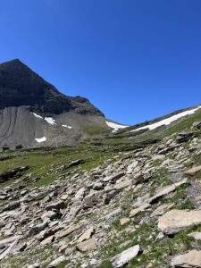 Steinige Hänge und letzte Schneefelder unterhalb der Felswand auf der Wanderung Grindelwald First–Axalp.