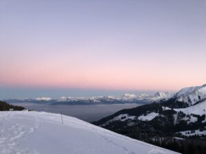 Breites Winterpanorama vom Gurnigel Richtung Alpenkette während der Rundwanderung Selibühl; zartrosa Morgen- oder Abenddämmerung über dem verschneiten Bergland.