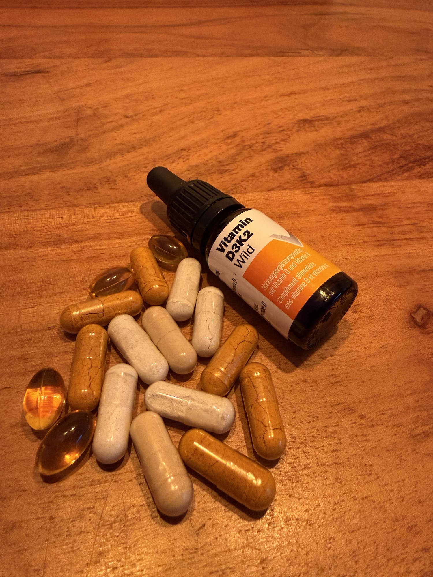 Verschiedene Supplements in Kapsel- und Ölform, darunter Vitamin D3/K2, auf einem Holztisch