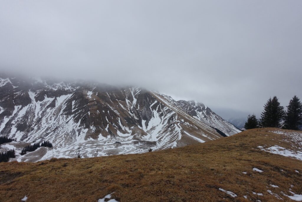 Winterliche Berglandschaft oberhalb des Schwarzsees mit schneebedeckten Hängen und tief hängenden Wolken im Naturpark Gantrisch