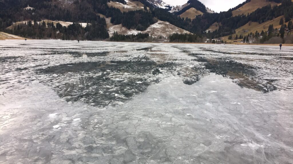 Zugefrorener Schwarzsee im Winter mit spiegelndem Eis und umliegenden Berghängen im Naturpark Gantrisch