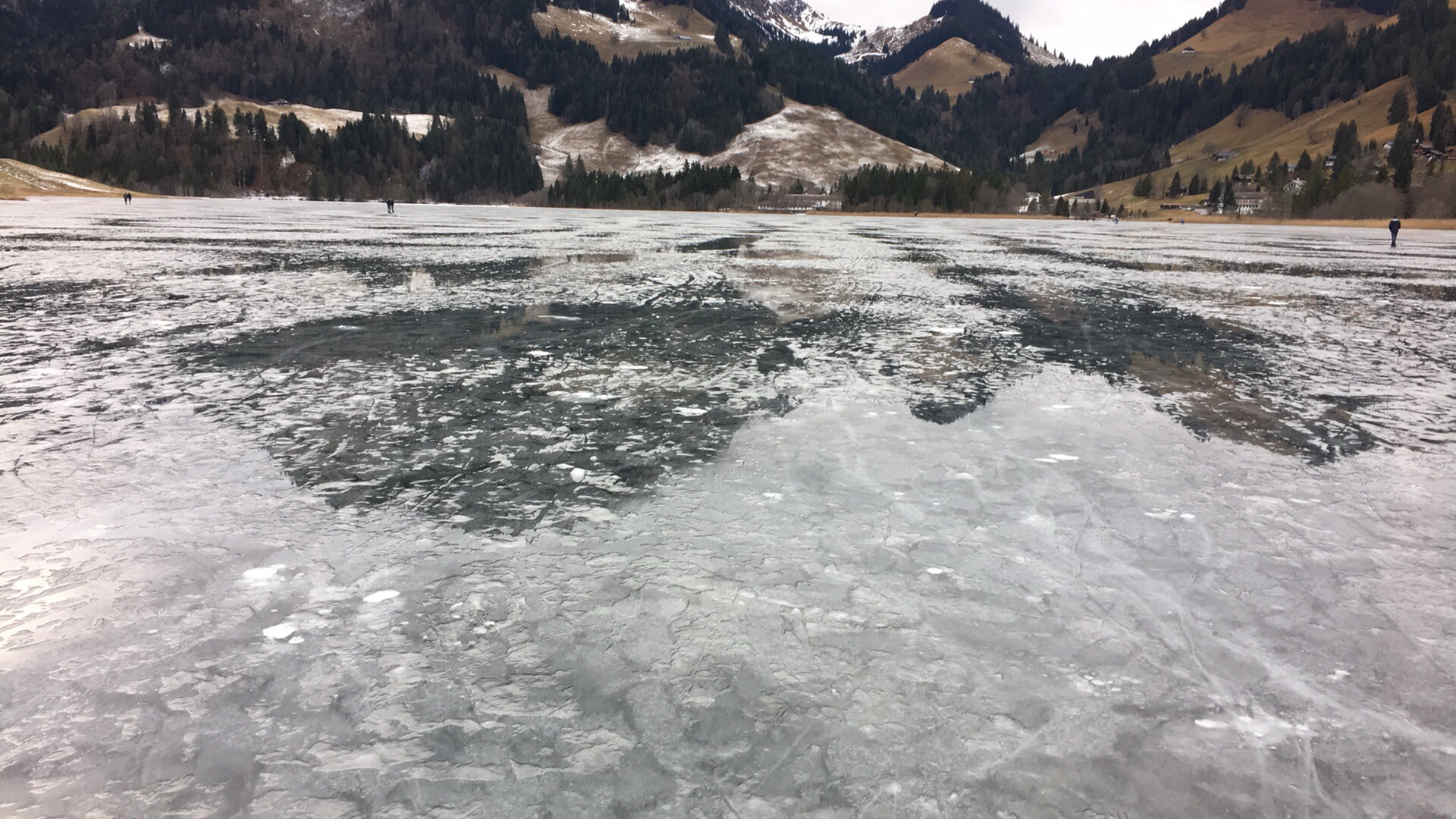 Zugefrorener Schwarzsee im Winter mit spiegelndem Eis und umliegenden Berghängen im Naturpark Gantrisch