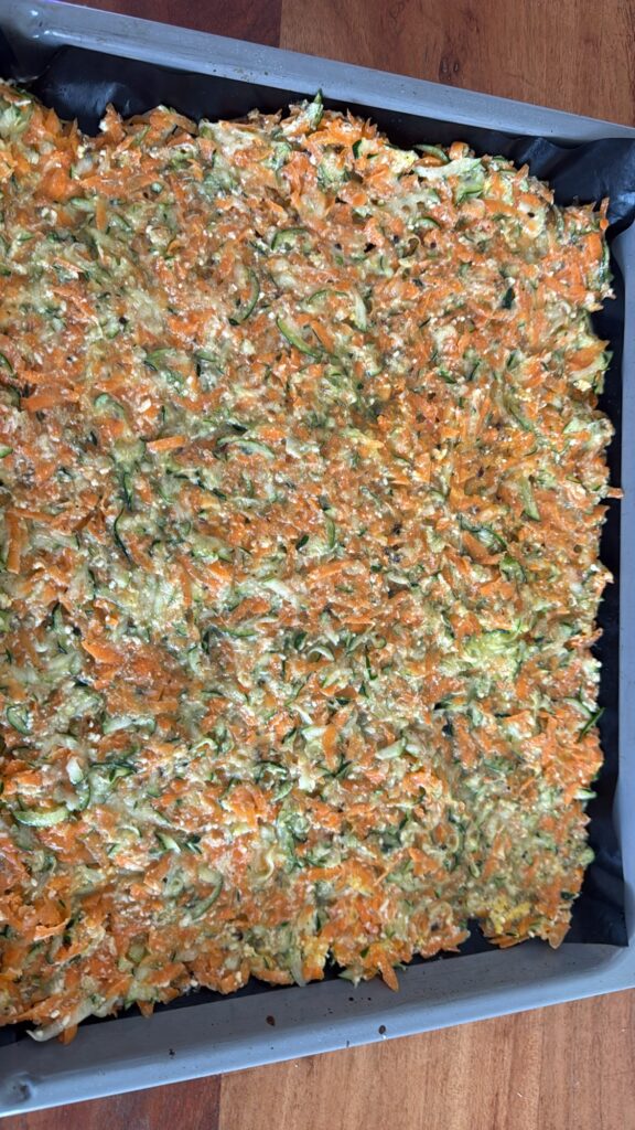 Zucchini-Karotten-Boden auf Backblech vor dem Backen, aus frisch geraffelten Zucchini, Karotten, Eiern und Käse als gesunde Low-Carb-Pizza-Alternative