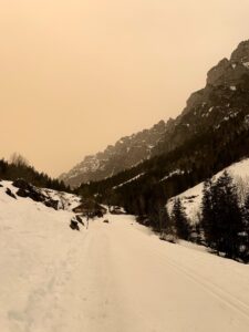 Präparierter Winterwanderweg durch das verschneite Justistal mit Alphütten und steilen Felswänden im Hintergrund.